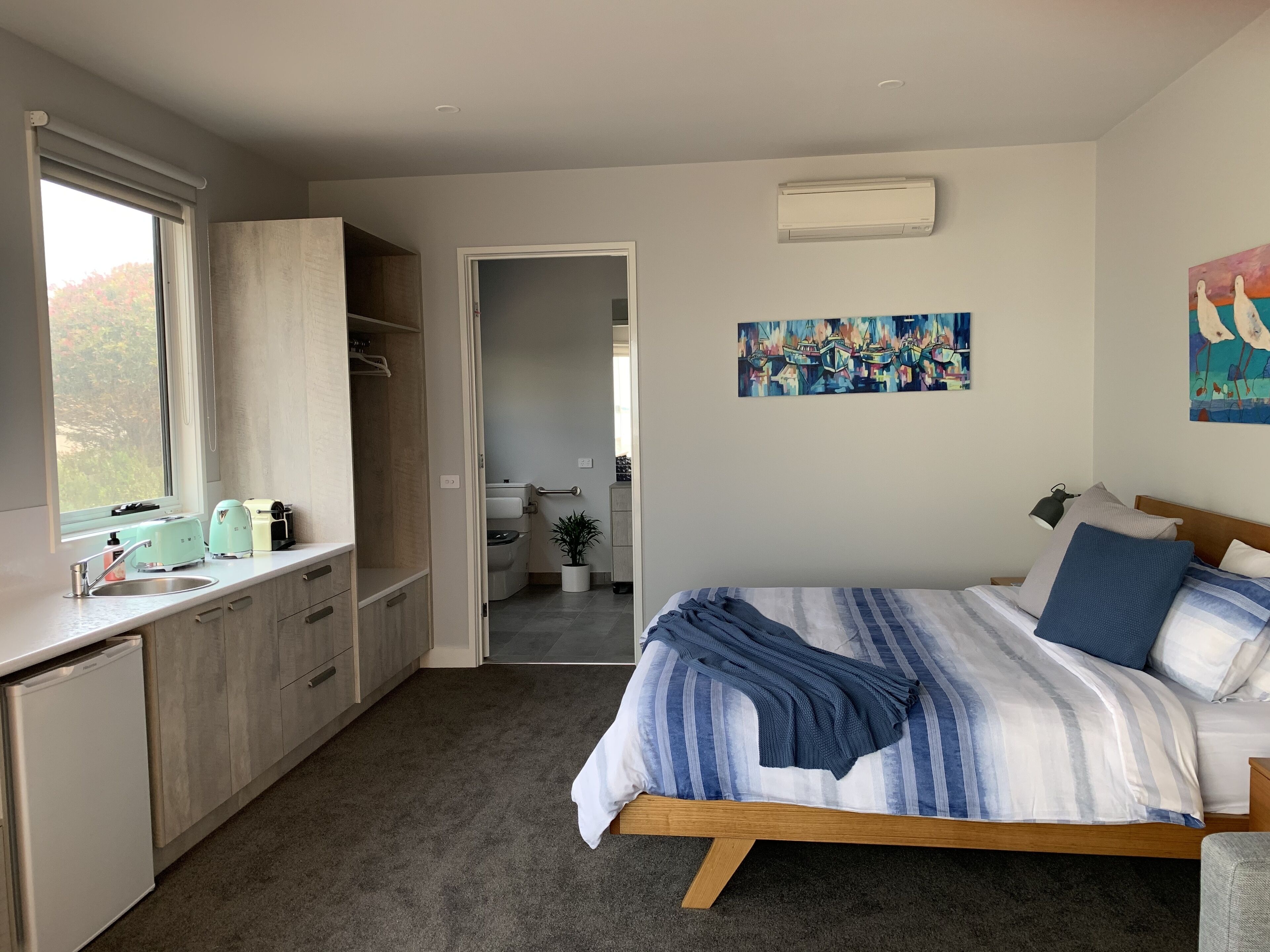 A bedroom with a bed, a bedside table, a window, a wardrobe, and a bathroom visible through an open door.