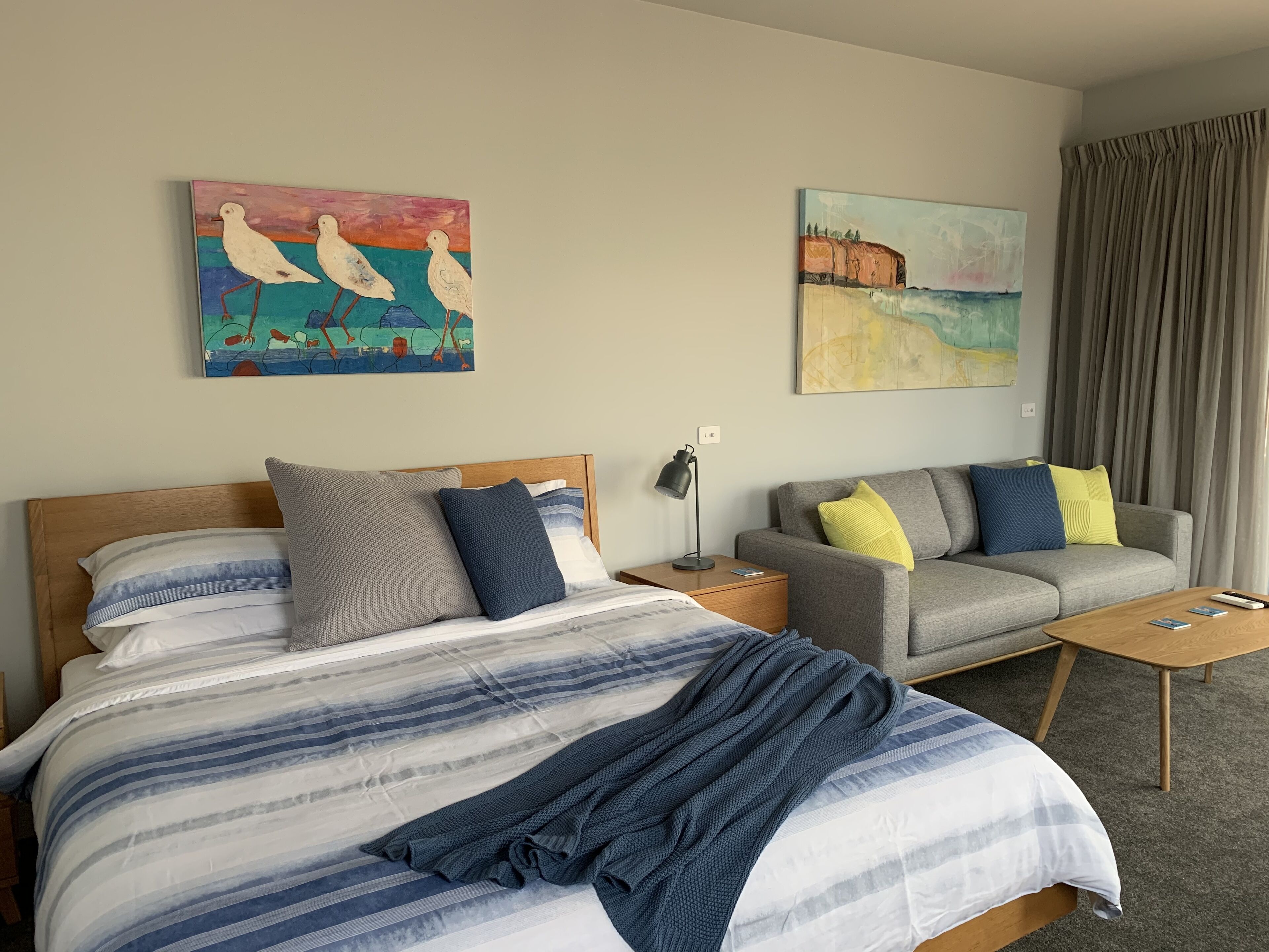 A hotel room with a bed, a sofa, a nightstand, and two paintings on the wall.
