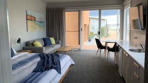 Habitación de hotel moderna con cama, sofá, mesa de comedor y zona de cocina.