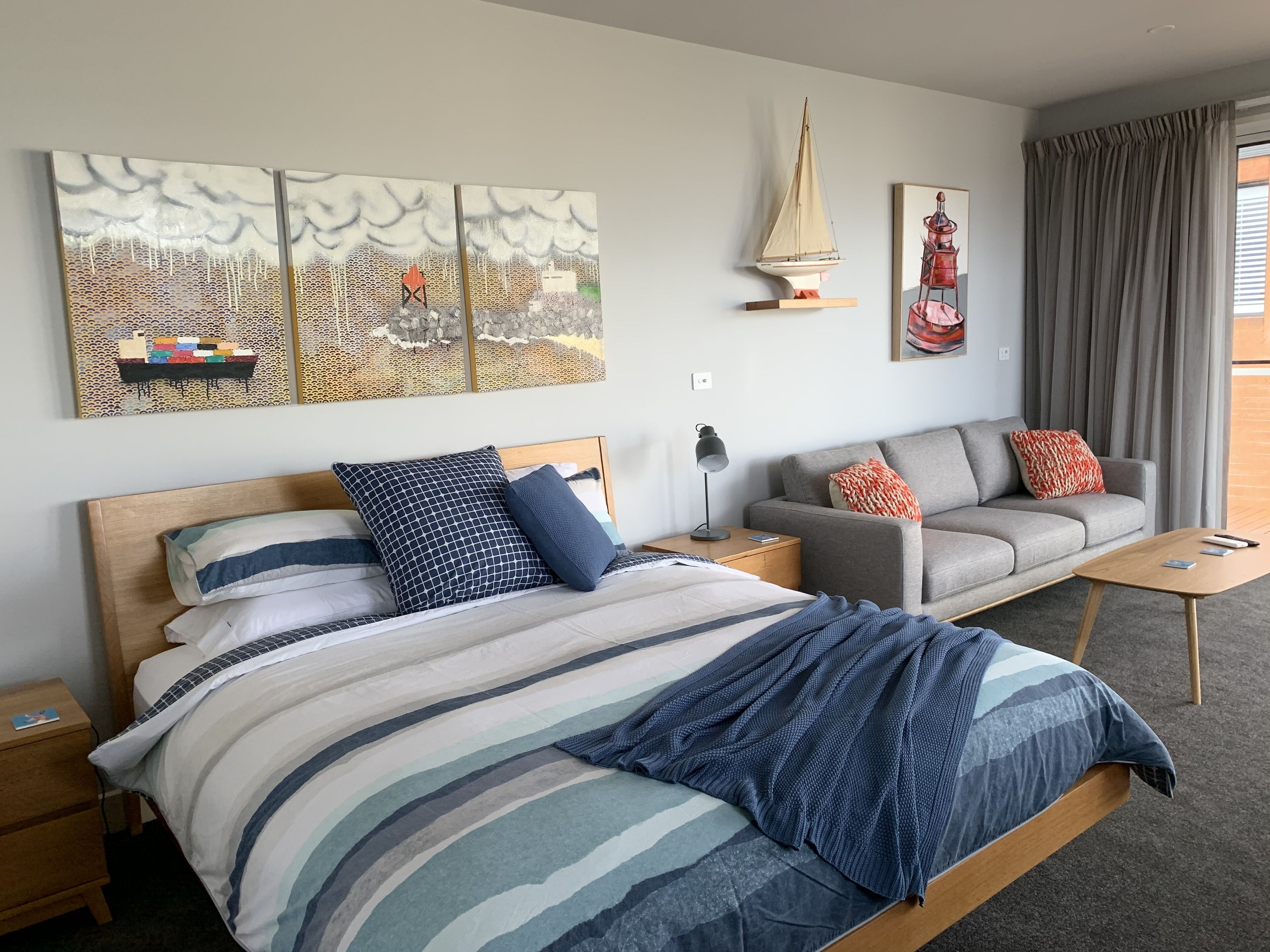 Una habitación de hotel moderna con una cama, un sofá, una mesita de noche, una lámpara y obras de arte en las paredes.