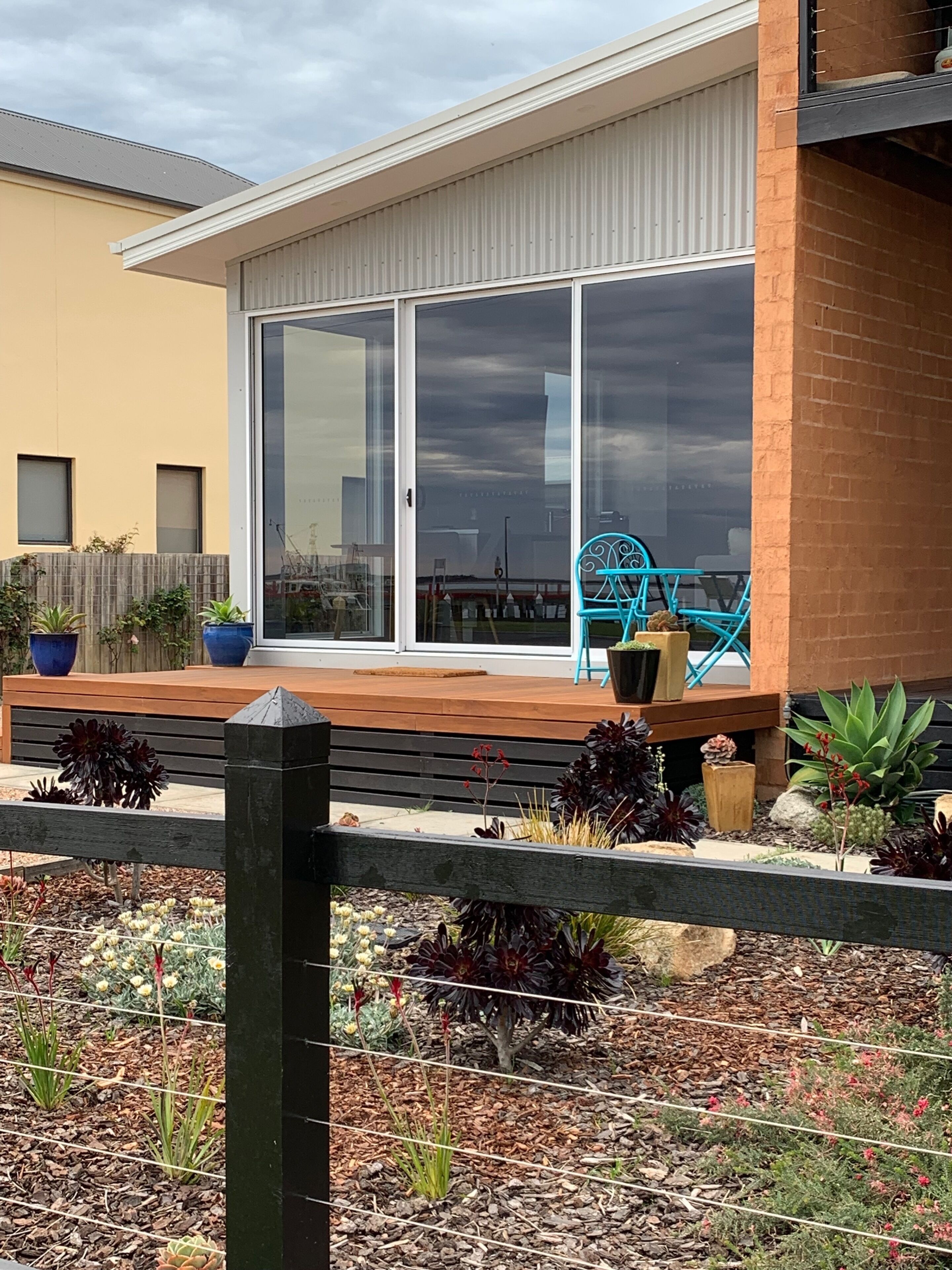 Een moderne patio met een schuifpui, een houten terras en diverse plantenpotten.