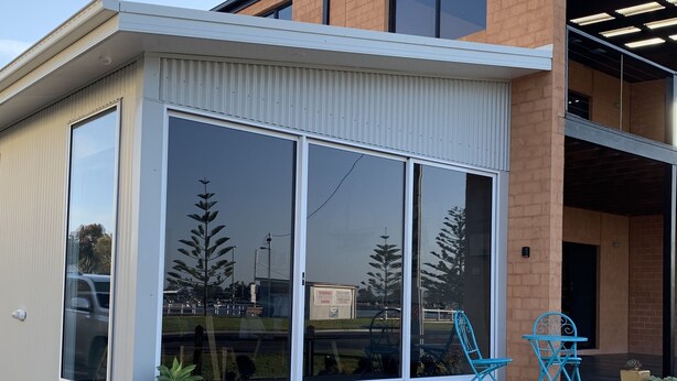 Una casa moderna con amplios ventanales correderos, una terraza de madera y mobiliario exterior.