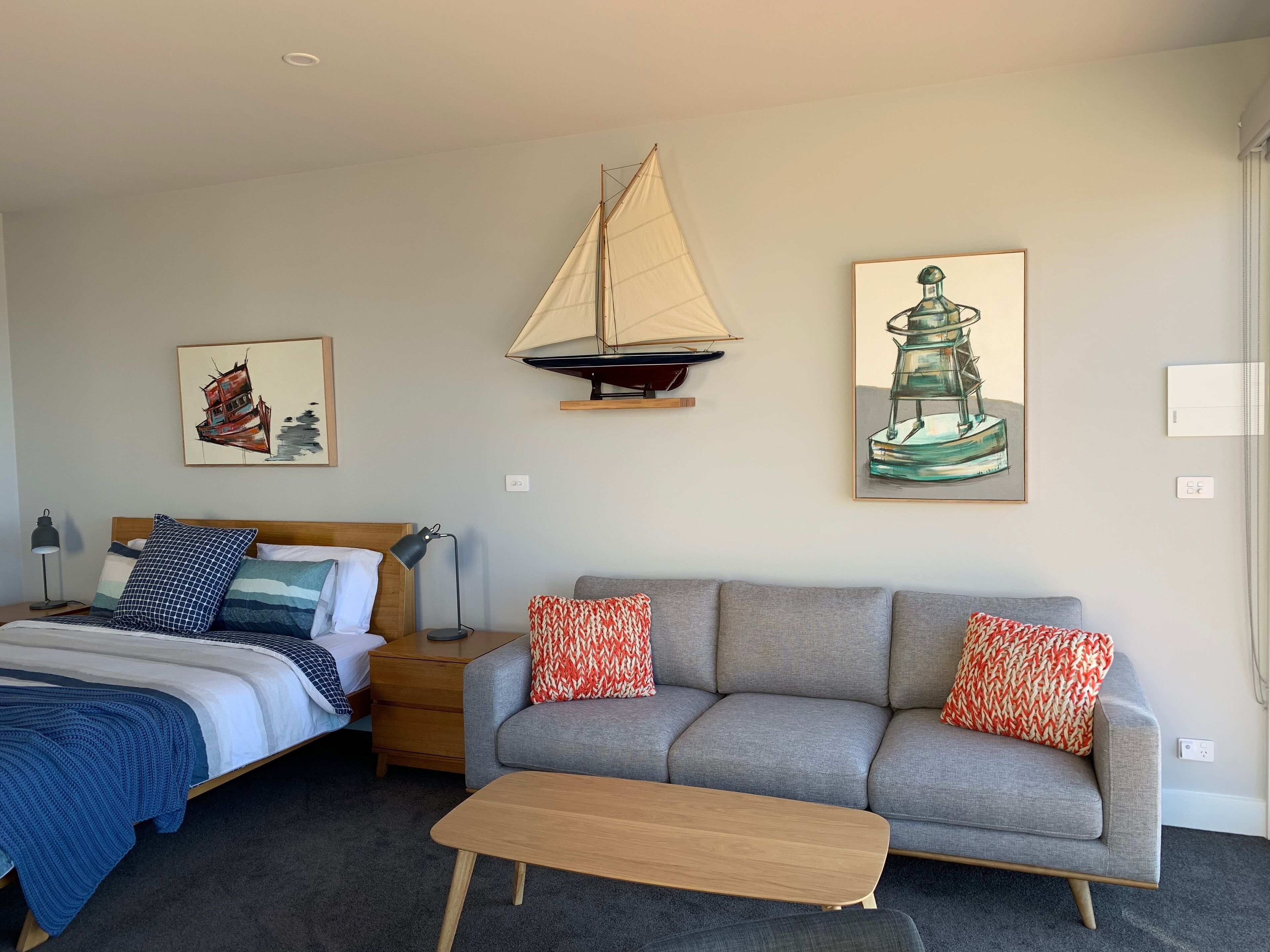 A hotel room with a bed, a gray sofa, a wooden bench, and two paintings on the wall.