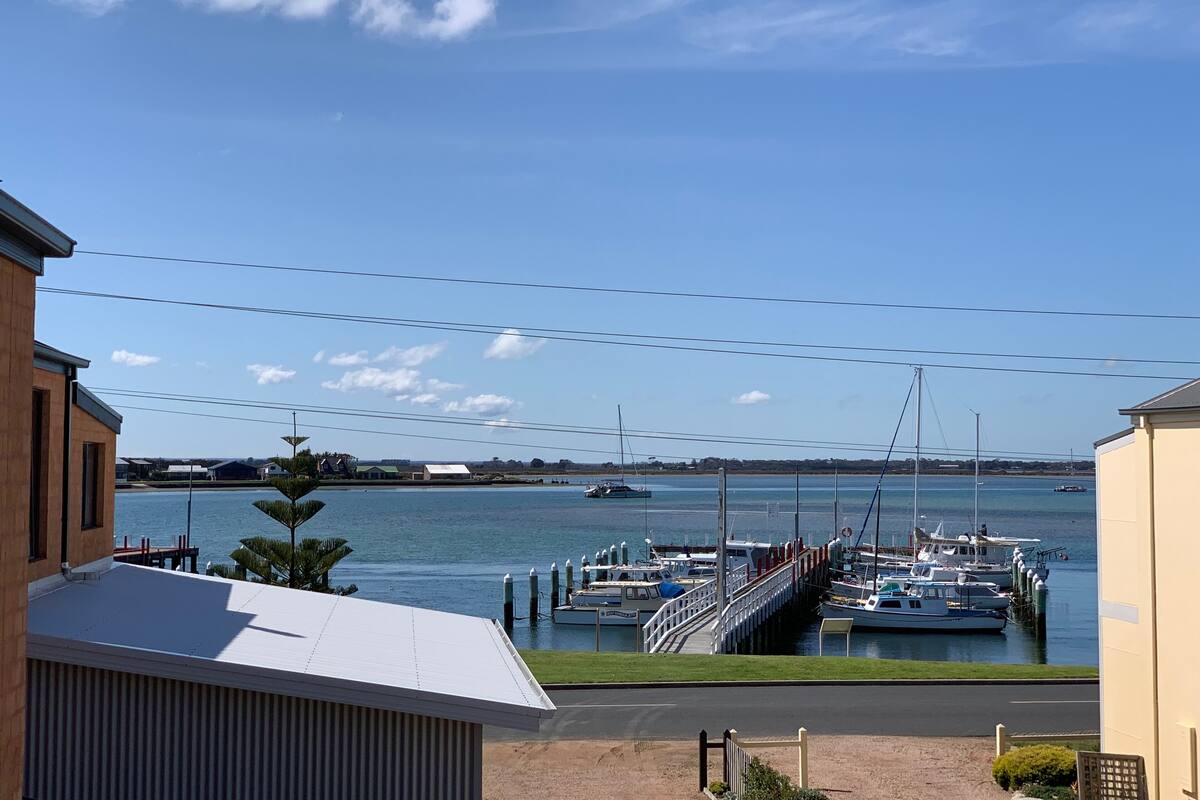 A marina with boats docked, a bridge, and buildings in the background.