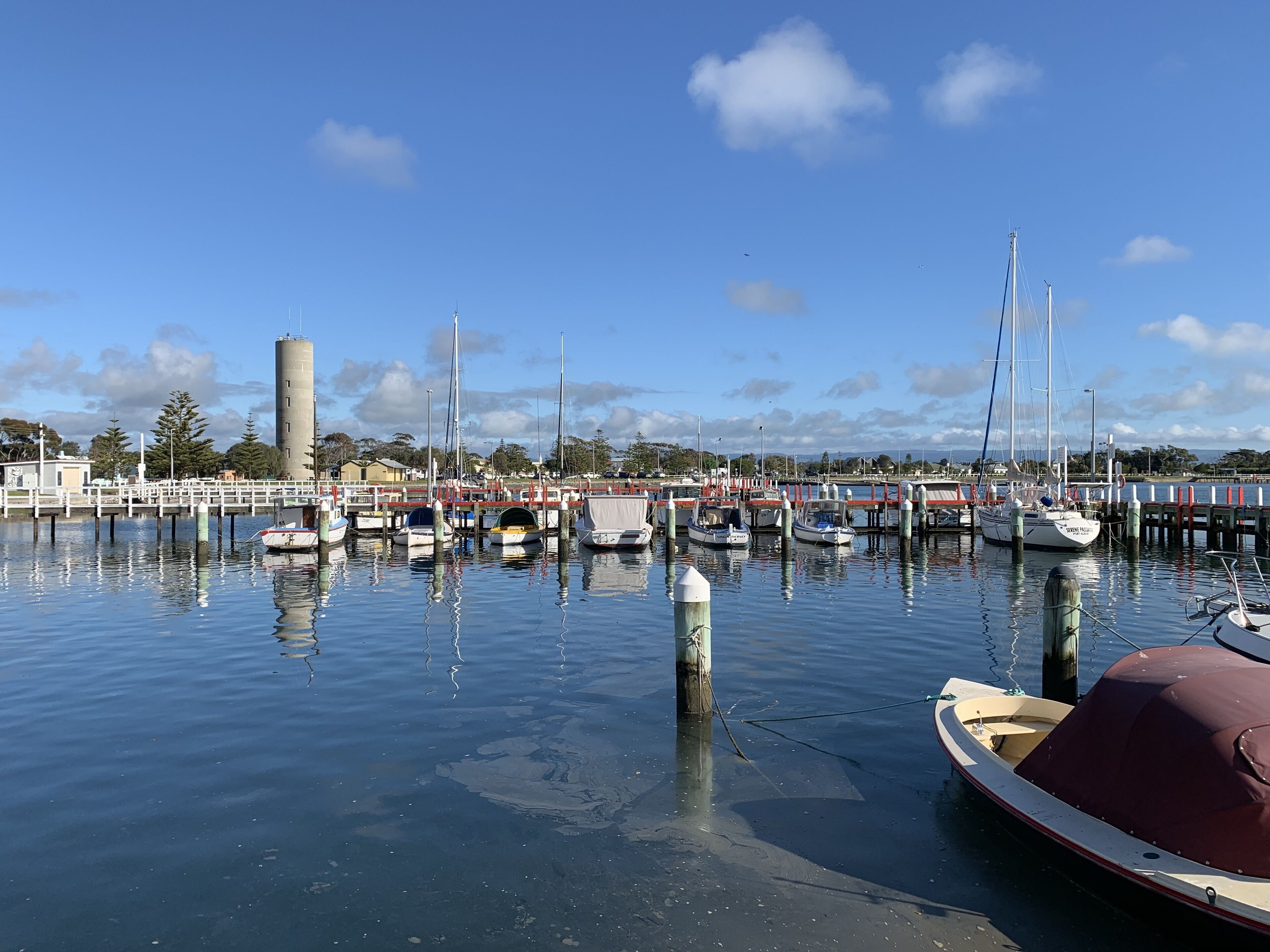 A marina with various boats docked, a bridge, and a water tower in the background.