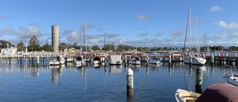 A marina with various boats docked, a bridge, and a water tower in the background.