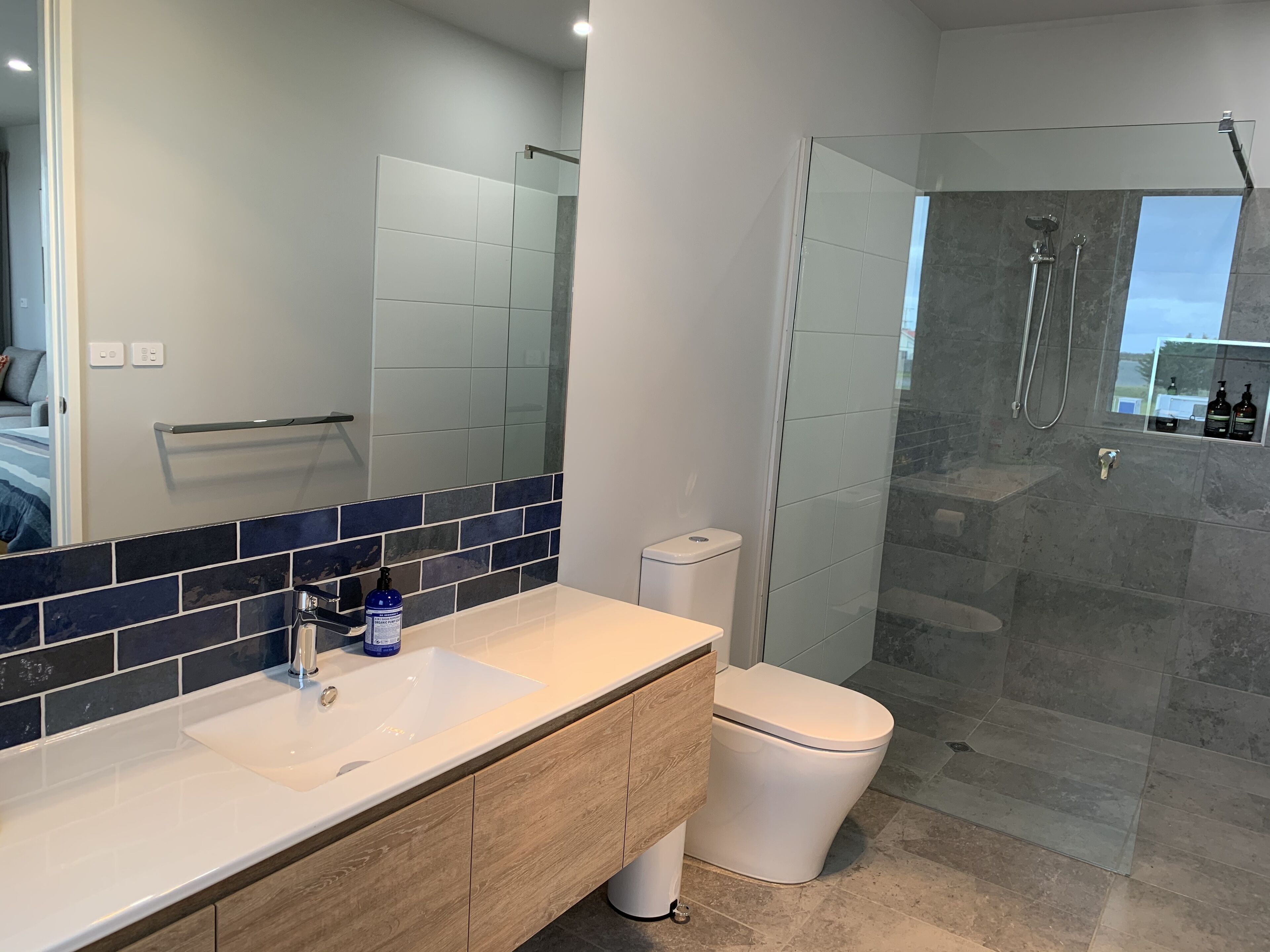 A modern bathroom with a white sink, wooden vanity, a glass shower enclosure, and a toilet.