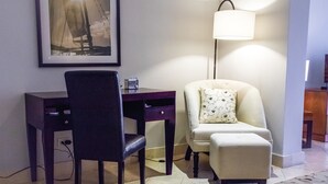 Ein Zimmer mit Schreibtisch, Stuhl, Lampe und einem gerahmten Bild an der Wand.