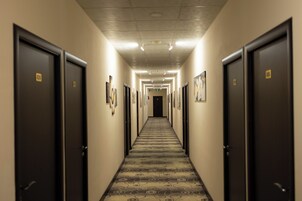 Un pasillo de hotel con puertas a ambos lados, alfombra estampada y cuadros en las paredes.