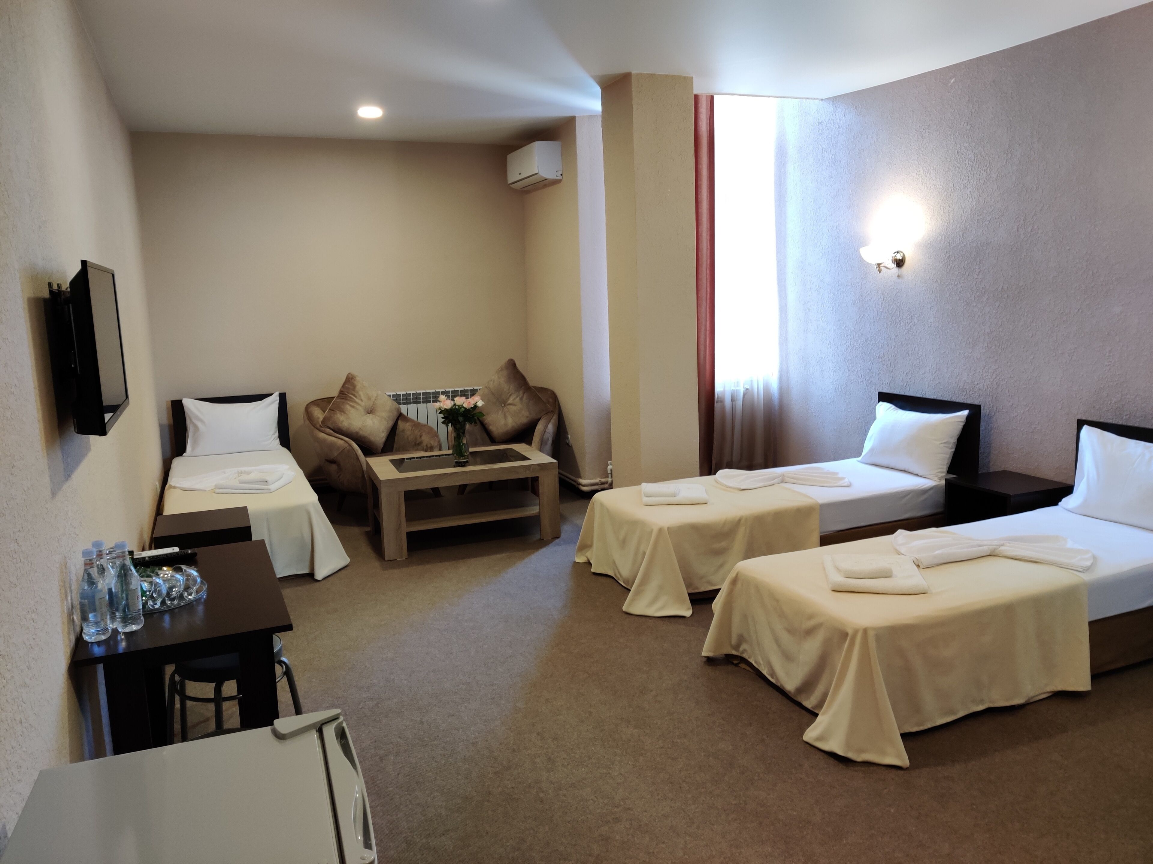 A hotel room with two single beds, a sofa, a small table, a TV, and a minibar.