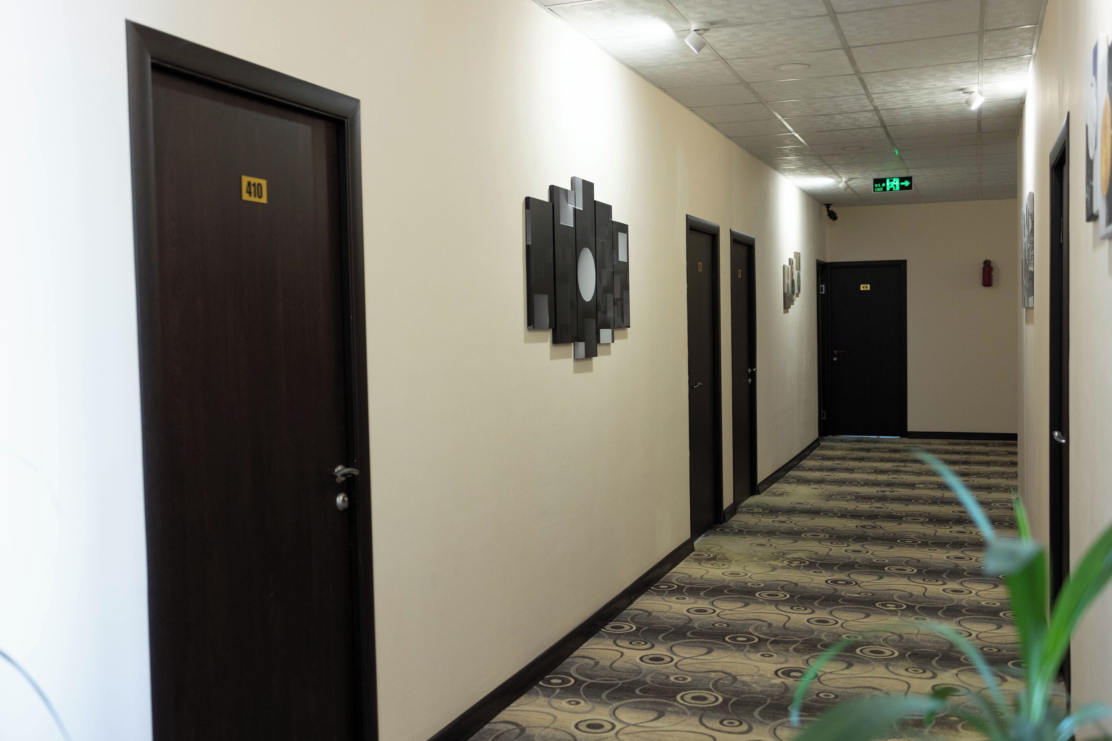 Un pasillo de hotel con puertas numeradas 410, 411 y 412, una alfombra estampada e iluminación empotrada en el techo.