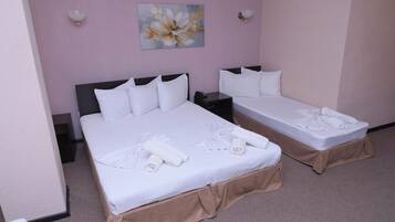 Two single beds with white linens and towels, a painting of a flower on the wall, and a beige carpet.
