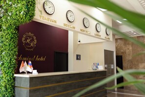 Een hotel receptiebalie met klokken die tijden uit verschillende steden aangeven, een balie versierd met vlaggen, en een logo met de initialen 'HR'.