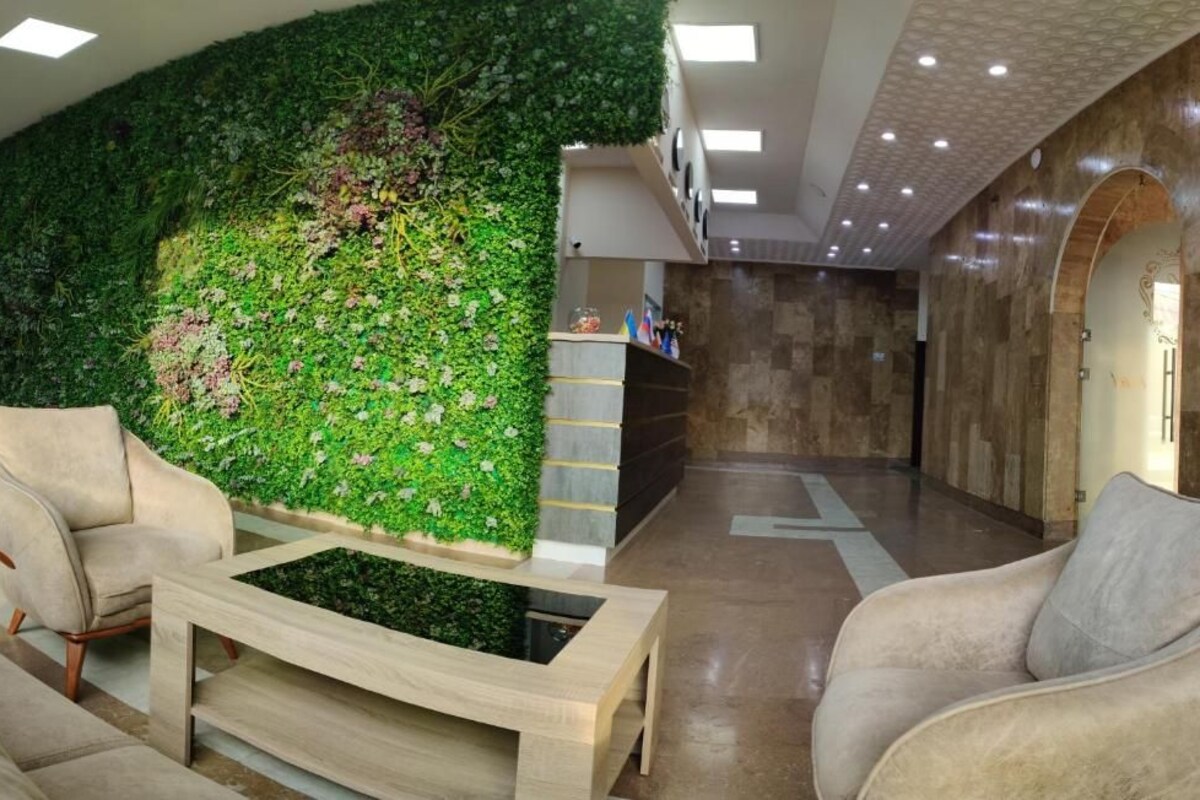 Un vestíbulo con un jardín vertical verde, una recepción y un área de estar con sofás y una mesa de centro.