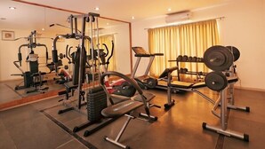A well-equipped gym with various exercise machines, a bench, and a rack of dumbbells. - Mayur aaditya resort (Dharwad)