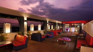 A rooftop bar with seating areas, including red and blue cushioned chairs and tables, under a purple sky. - Mayur aaditya resort (Dharwad)