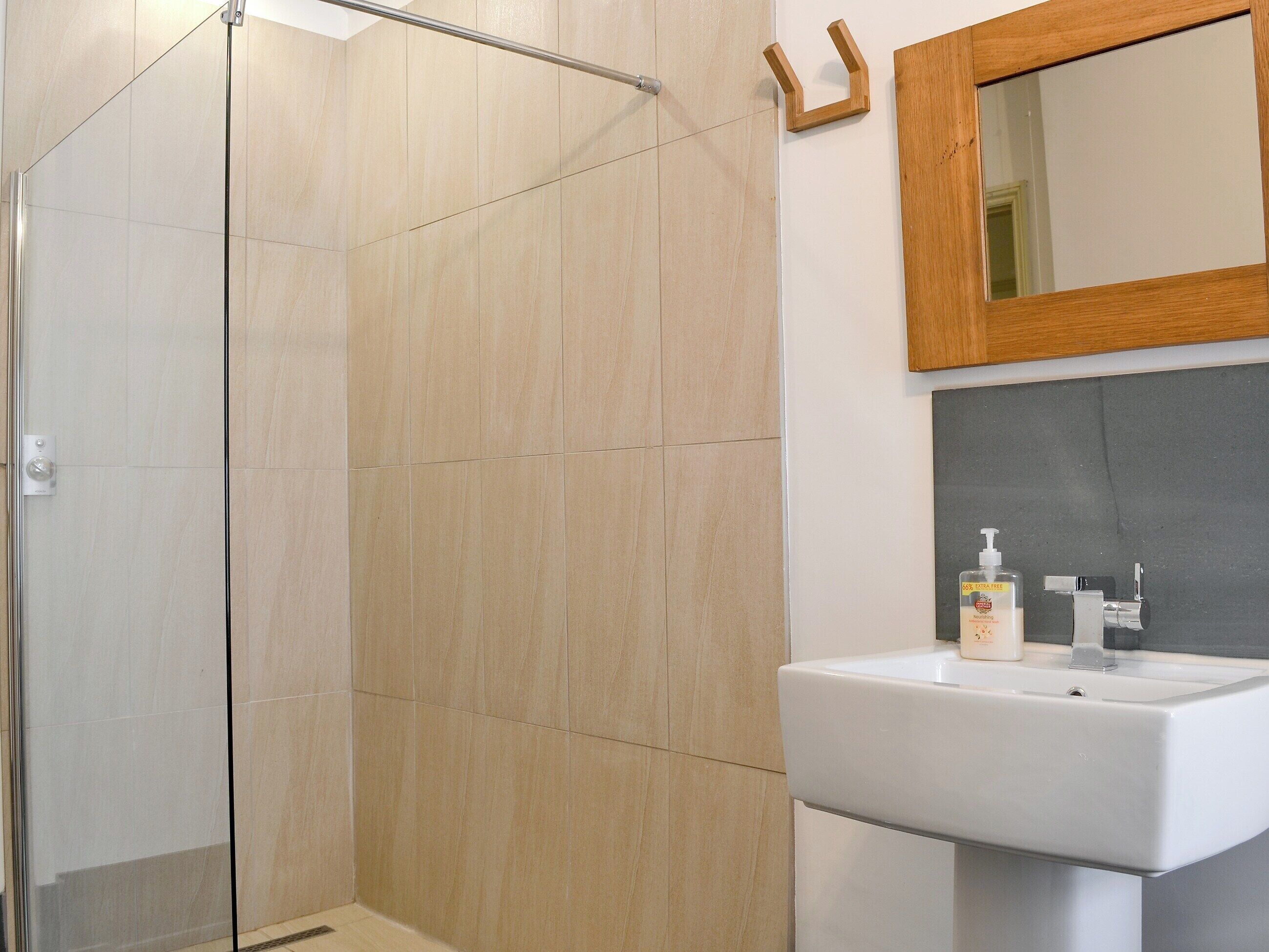 Un bagno moderno con box doccia in vetro, uno specchio con cornice in legno e un lavandino bianco con dispenser per sapone.