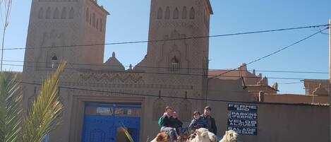 A building with two towers and a blue door, with people and camels in front.