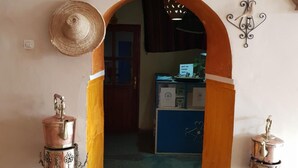 An arched doorway with a decorative hat on the left, two metal containers on pedestals, a clock, and a wall-mounted sign above. - Gîte Kasbah La palmeraie (Skoura)