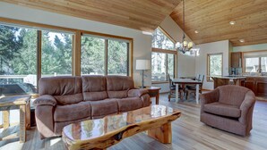 A spacious living room with a large brown leather sofa, a wooden coffee table, and a dining area with a wooden table and chairs. - 15 Big Leaf - Remodeled, Grassy Lawn, Fabulous Location, SHARC Passes, A/C (Bend)