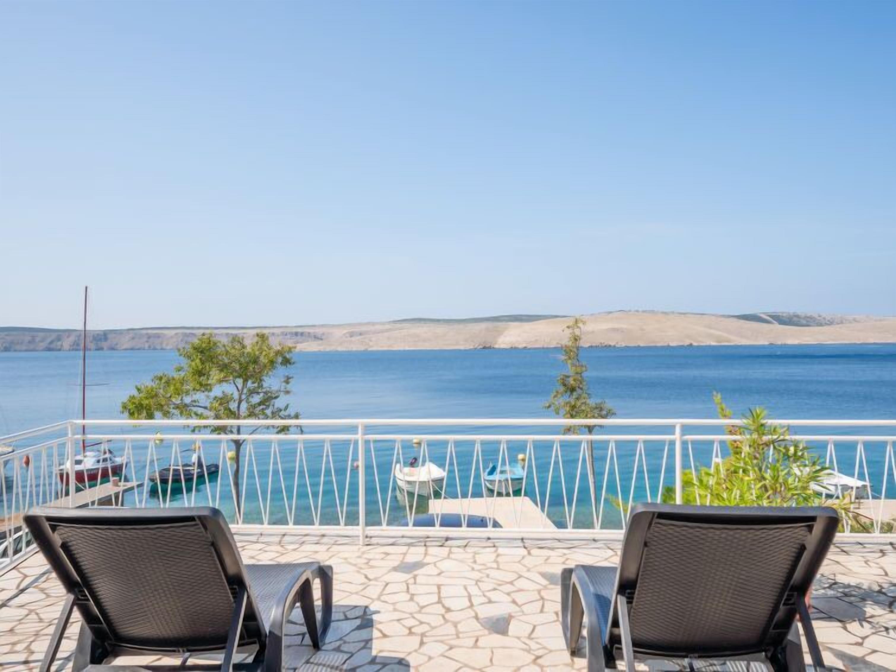 A balcony with two chairs, a pool, and a view of the sea and hills.