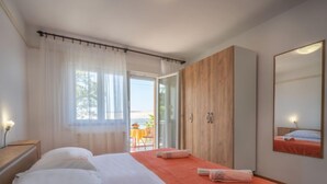 Une chambre avec deux lits, une armoire en bois, un grand miroir et un balcon avec une table et des chaises.