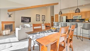 A spacious living area with a fireplace, a dining table with chairs, a kitchen with bar stools, and a ceiling fan. - Riverfront Silverthorne Condo Near Skiing! (Silverthorne)