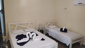 Et hotelværelse med to enkeltsenge, et natbord med lampe, en vægmonteret aircondition og en dør med håndtag.