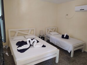 A hotel room with two single beds, a bedside table with a lamp, a wall-mounted air conditioner, and a door with a handle. - Hostal Yanelis & Harol (Trinidad)