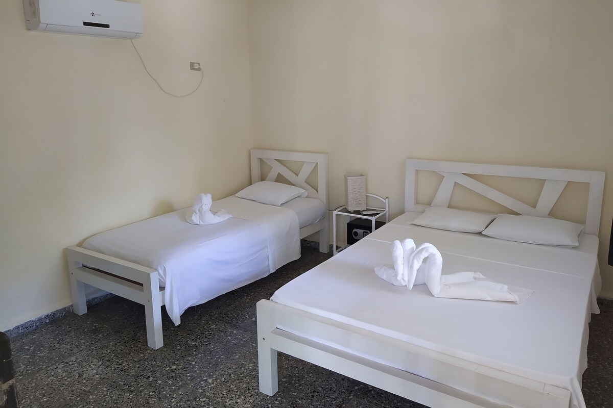A hotel room with two single beds, a small bedside table with a lamp, and a wall-mounted air conditioner.