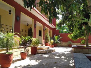 A building with a red and yellow facade, multiple potted plants, and a paved walkway. - Hostal Yanelis & Harol (Trinidad)