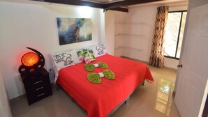 Een slaapkamer met een rood sprei, een decoratieve wandversiering, een bedlampje en een deur met gordijnen.