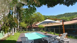 Un área de piscina con sillones de descanso y una pérgola que proporciona sombra.