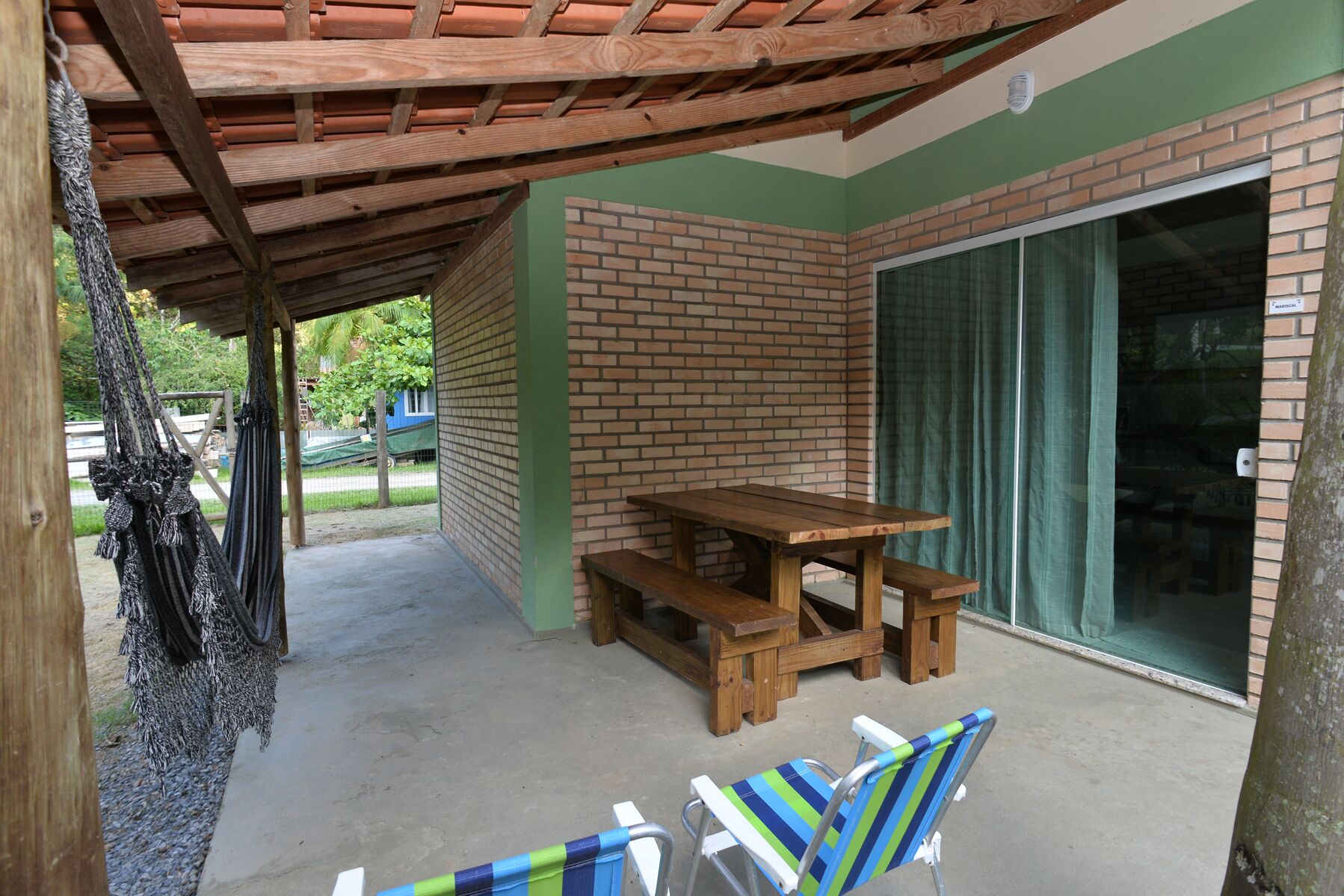 A covered patio area with a wooden table and benches, a sliding glass door, and two striped beach chairs.