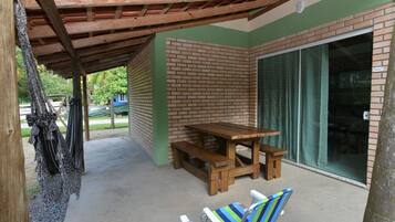 A covered patio area with a wooden table and benches, a sliding glass door, and two striped beach chairs.