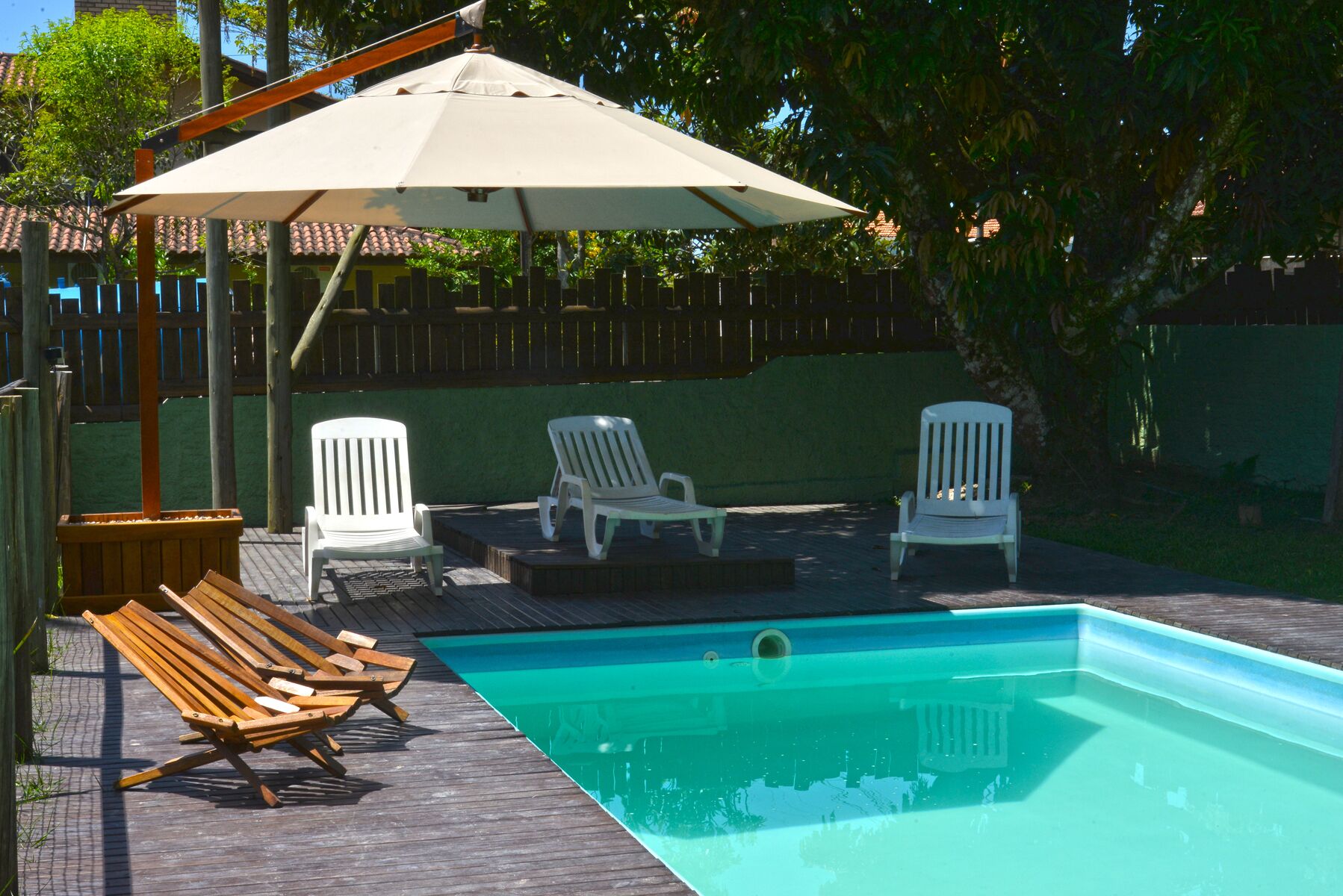 Piscina con sillones de madera y una sombrilla blanca.