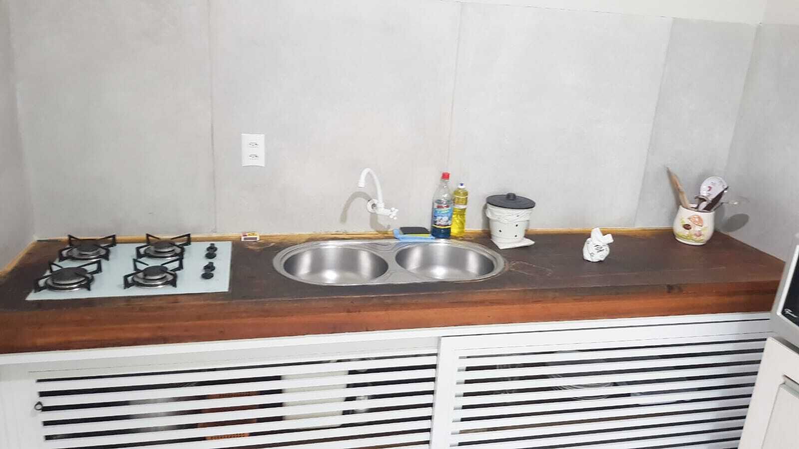 Une cuisine de taille réduite, équipée d’une cuisinière à gaz, d’un évier à deux bacs et d’un plan de travail en bois.