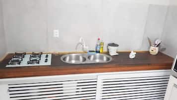 Une cuisine de taille réduite, équipée d’une cuisinière à gaz, d’un évier à deux bacs et d’un plan de travail en bois.