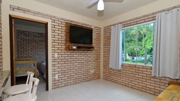 Una habitación con pared de ladrillo, un televisor de pantalla plana montado sobre un estante de madera, una ventana con cortinas y un ventilador de techo.