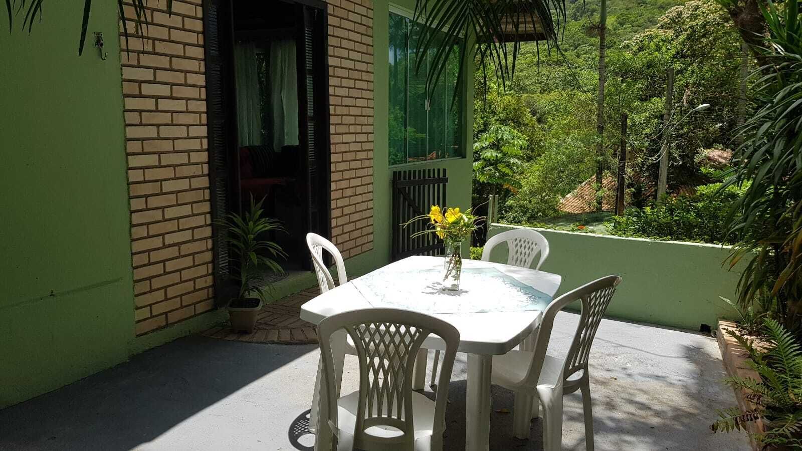 Eine Terrasse mit einem weißen Tisch und Stühlen, umgeben von Grünpflanzen und einer Backsteinmauer.
