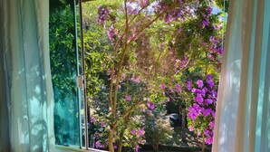 Una habitación con un ventanal grande, un sofá a rayas y vistas a árboles con flores moradas.