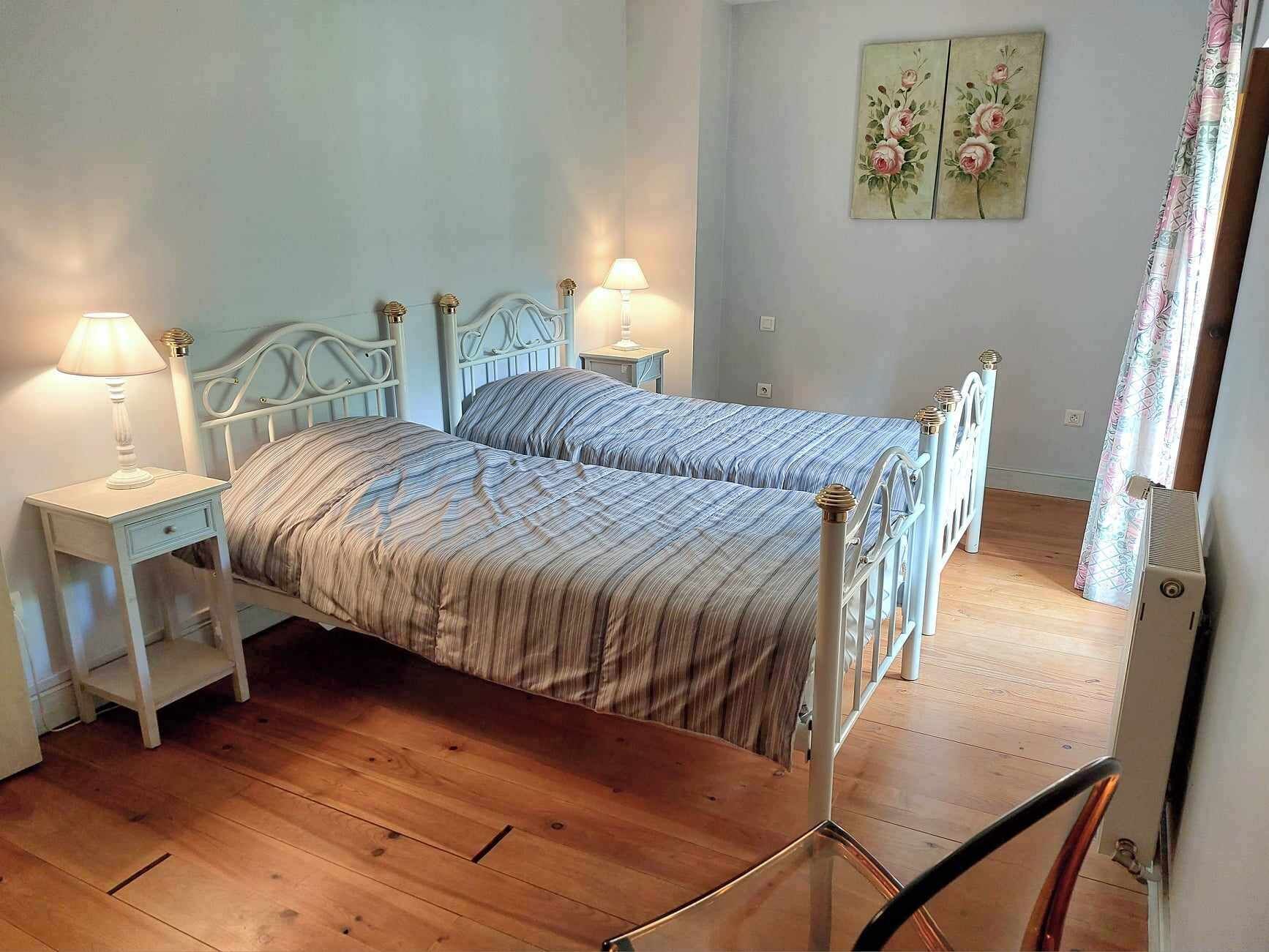 Un dormitorio con dos camas individuales, suelo de madera, mesitas de noche con lámparas y decoración floral en la pared.