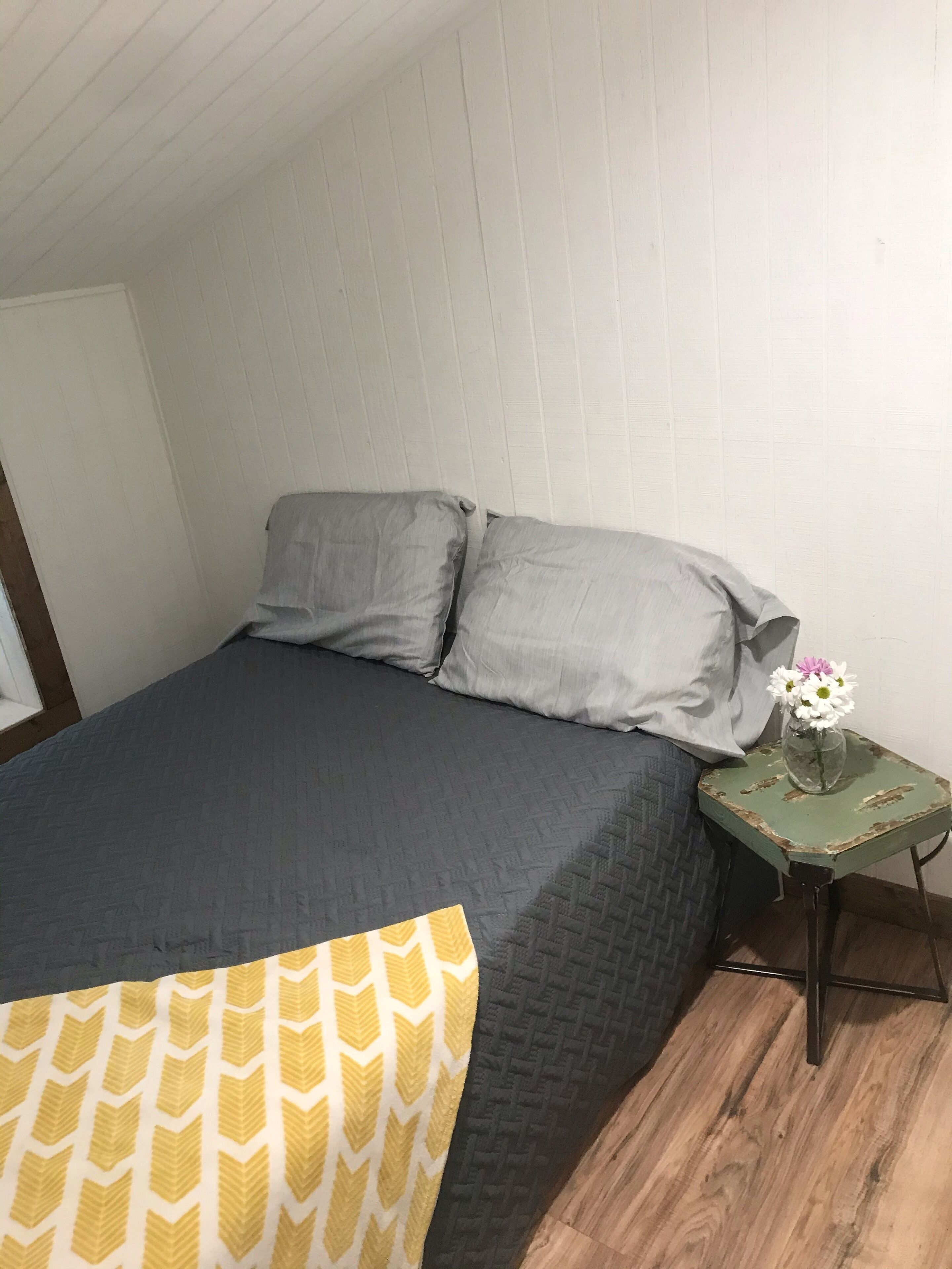 A bedroom with a bed, pillows, a nightstand, and a vase with flowers.