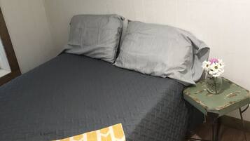 A bedroom with a bed, pillows, a nightstand, and a vase with flowers.