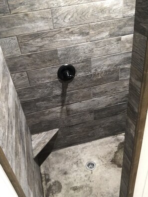 Une douche avec des carreaux de bois foncé et un robinet noir.