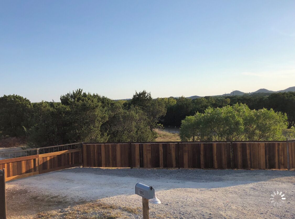 Un espacio al aire libre cercado con un buzón, suelo de grava y árboles al fondo.