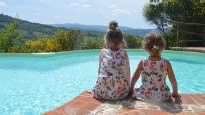 Deux enfants sont assis au bord d’une piscine, avec une vue sur des collines et des arbres.