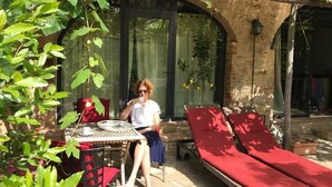 Un espace patio avec une table et des chaises, un fauteuil de relaxation rouge avec coussin, et une porte vitrée donnant sur un jardin.