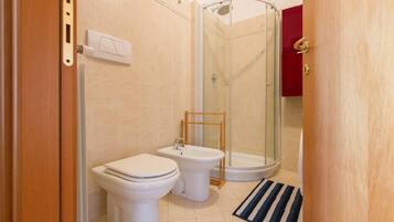 A bathroom with two toilets, a bidet, and a glass-enclosed shower.