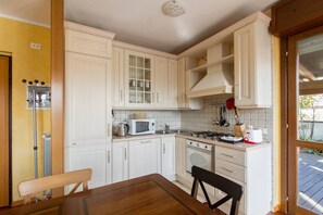 Een kleine keuken met witte kasten, een magnetron, een fornuis en een eettafel met stoelen.